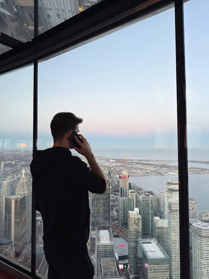 Marcel Sandro Truskaller, Geschäftsführer von Agentur.jetzt, telefoniert vor einer Glasfront über einer Stadt in der Abenddämmerung
